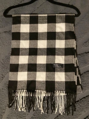 Rutig Burberry Halsduk - Burberry halsduk 🖤🤍  Klassisk Burberry-halsduk i det välkända rutmönstret. En tidlös favorit som aldrig går ur stil.  ✨ Detaljer: – Material: Lammull – Färg: Vit/Svart/Grå – Mått: 165 cm x 32 cm – Skick: Mycketbra – Original: ja  Perfekt till höst & vinter och funkar både casual och uppklätt. Skickas snabbt 📦  Pris kan diskuteras.