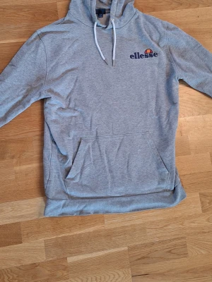 Grå hoodie från Ellesse - Snygg grå hoodie från Ellesse med broderad logga på bröstet. Klassisk känguruficka framtill och vita dragsnören i huvan. 