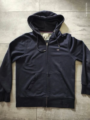 Gant Zip hoodie - GANT huvtröja med dragkedja – marinblå, strl S  Snygg och klassisk huvtröja från GANT i mörk marinblå färg. Tröjan har dragkedja framtill, justerbar huva med snören samt broderad GANT-logga på bröstet. Mjuk och bekväm kvalitet, perfekt för vardagsbruk. Använt ett fåtal gånger.