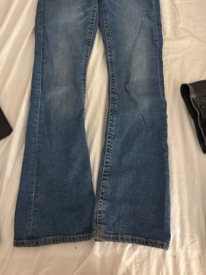 Blå bootcut jeans med slitningar - Snygga blå bootcut jeans med lätt slitna detaljer och klassiska fickor bak. Jeansen har en något utsvängd passform nertill och är tillverkade i denim. Perfekta för en avslappnad och trendig look.