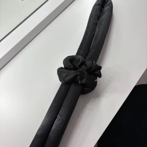 Svart satin värmerulle & scrunchies set - Snyggt set med en svart värmerulle för håret och tre matchande scrunchies i glansigt satintyg. Perfekt för att skapa lockar utan värme och samtidigt hålla håret på plats med stil. Enkel att använda och skonsam mot håret.