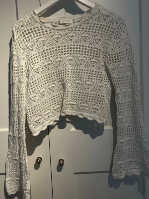 Vit virkad stickad tröja Monki - Säljer en vit virkad stickad tröja från Monki med lång ärm och utsvängda ärmslut. Tröjan har ett genombrutet mönster och är något croppad i modellen. Perfekt för dig som gillar boho-vibbar och vill ha något luftigt och snyggt.