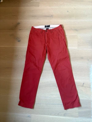 Röda chinos från Abercrombie & Fitch - Snygga röda chinos från Abercrombie & Fitch i modellen slim straight. Byxorna har klassisk passform med fickor i sidorna och bak, samt knapp och dragkedja i gylfen. Perfekta för en stilren och avslappnad look. 