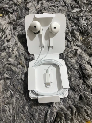 Apple EarPods med Lightning-kontakt - Säljer ett par vita Apple EarPods med Lightning-kontakt. Klassisk design med rundade öronsnäckor och sladd i tålig plast. Perfekta för iPhone-användare som vill ha bra ljud och smidig passform. Levereras i originalförpackning.