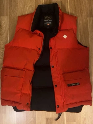 Röd dunväst från Canada Goose - Snygg röd dunväst från Canada Goose med klassisk passform och två stora framfickor. Västen är självklart äkta👍 Bara skriva för fler frågor. 