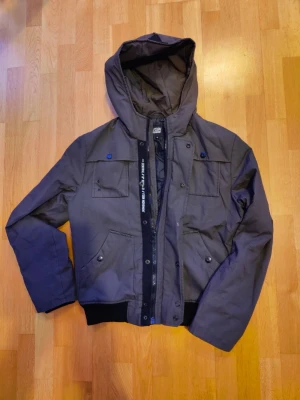 Jacka från Fishbone - Jacka från Fishbone med huva och dragkedja. Jackan har fickor framtill och ribbad mudd nedtill. Snygg detalj med text på dragkedjans kant. 