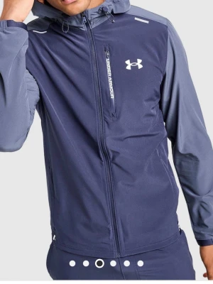 Blå träningsjacka från Under Armour - Sportig blå träningsjacka från Under Armour med huva, dragkedja och bröstficka. Jackan har logga på bröstet och elastiska muddar. Tillverkad i ett lätt och funktionellt material som passar perfekt till träning utomhus.