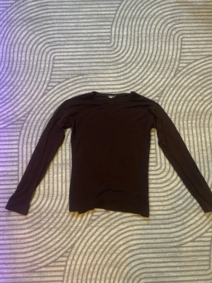 Brun långärmad topp i bomull - Mörkbrun långärmad topp med enkel och stilren design. Tillverkad i mjuk bomull som känns skön mot huden. Perfekt basplagg att matcha med olika outfits. Rund halsringning och normal passform.