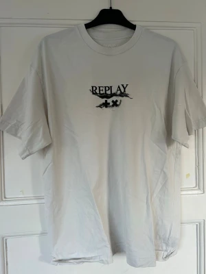 Vit Replay x Martin Garrix t-shirt - Snygg vit t-shirt från Replay i samarbete med Martin Garrix. T-shirten har svart tryck på bröstet och är tillverkad i mjuk bomull. Klassisk passform med rund hals och korta ärmar. Perfekt för en avslappnad och trendig stil.