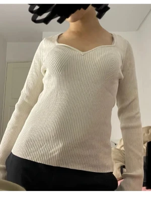 Vit ribbad stickad tröja - Säljer en vit, ribbad stickad tröja med lång ärm och markerad sweetheart-urringning. Tröjan har figurnära passform och är tillverkad i ett mjukt, stretchigt material som sitter snyggt på kroppen. Passar för dig som har S i storlek också🩷