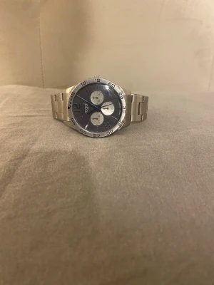 Silverfärgad klocka från Regal - Stilren klocka från Regal med silverfärgad länkarmband och svart urtavla. Klockan har tre mindre vita urtavlor och tydliga siffror i vitt. Perfekt accessoar för dig som gillar en klassisk men modern look.