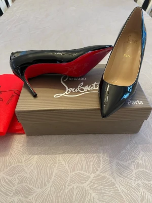 Svarta lackpumps Christian Louboutin-lika - Snygga svarta pumps i lack Christian Louboutin lika med klassisk spetsig tå och ikonisk röd sula. Skorna har hög klack och elegant form, perfekta för att lyfta vilken outfit som helst.