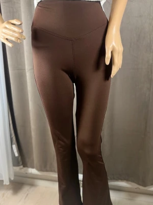 Bruna utsvängda mjukisbyxor - Mörkbruna mjukisbyxor med hög midja och utsvängda ben. Byxorna har en slät och stretchig passform som sitter bekvämt. Perfekta för en avslappnad och trendig stil.