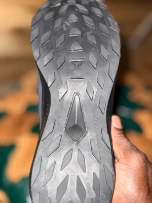 Svarta sneakers från Salomon - Säljer ett par svarta löparskor från Salomon med slitstark gummisula och grovt mönster för bra grepp. Ovandelen är i meshmaterial som andas och har diskreta detaljer. Perfekta för löpning eller träning utomhus.