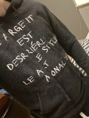 Mörkgrå hoodie med vit text - Säljer en mörkgrå hoodie med vit handskriven text på framsidan. Hoodien har huva med dragsko och en klassisk magficka. Perfekt för dig som gillar streetwear och vill sticka ut med ett unikt tryck.