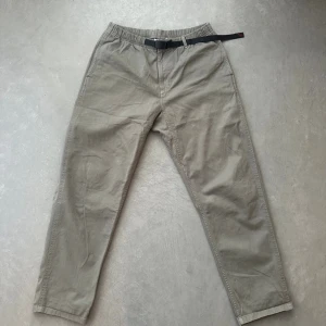 Beige chinos från Gramicci  - Snygga beige chinos från Gramicci med elastisk midja och inbyggt svart bälte. Byxorna har raka ben och två sidofickor. Perfekta för en avslappnad och trendig stil. Materialet är mjukt och bekvämt bomullstyg. Köpt på Vallgatan 12 för några månader sedan. Bra skick inte använd många gånger. 