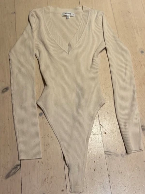 Beige ribbad body  - Snygg beige body med lång ärm och djup V-ringning. Perfekt att styla med jeans eller kjol för en clean look.