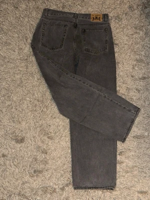 Grå sweetsktbs jeans  - Säljer ett par grå jeans från Junkyard 30/30 med raka ben och klassiska bakfickor. Jeansen har en vintagekänsla och är tillverkade i bomull. Perfekta för en avslappnad och stilren look.