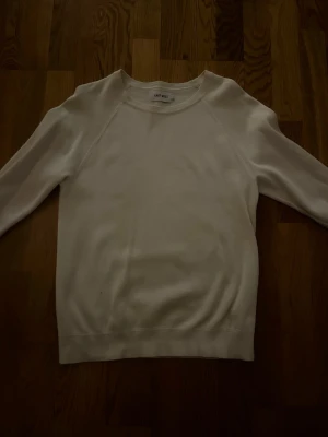 Vit tröja från EAST WEST - Klassisk vit tröja från EAST WEST i storlek S. Tröjan har rund halsringning, långa ärmar och ribbade muddar vid ärmslut och nederkant. Enkel och stilren design som passar till det mesta. Perfekt basplagg i garderoben.