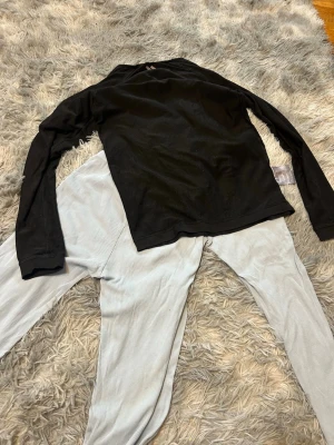 Svart långärmad pyjamastopp & ljusa byxor - Mysig pyjamas med svart långärmad tröja och ljusa, ribbade byxor. Perfekt för att chilla hemma eller sova bekvämt. Tröjan har enkel design och byxorna har resår i midjan för extra komfort.