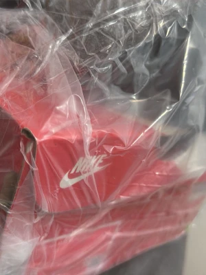Nike sneakers i röd originalkartong - Säljer ett par Nike sneakers i sin klassiska röda originalkartong med vit logga. Perfekt för dig som gillar sportig och stilren design från ett av världens mest ikoniska märken.