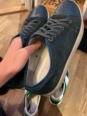 Lanvin cap toe - Snygga mörkblå sneakers från Lanvin med ovandel i mocka och detaljer i blankt läder på tån och runt öppningen. Skorna har grå snörning och vit sula. Perfekta för dig som gillar stilrena och exklusiva sneakers.