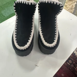Svarta boots med vit stickad kant 37  - Säljer ett par svarta boots med grov sula och vit stickad kant runt öppningen. Insidan är fodrad med mjukt material för extra värme. Skorna har en högre modell och är perfekta för kyligare dagar. Klassisk och mysig look med kontrastfärgade detaljer.