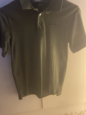 Olivgrön Peak Performance piké S - Säljer en stilren olivgrön pikétröja från Peak Performance i storlek S. Klassisk krage, korta ärmar och knappar framtill. Diskret logga på bröstet. Perfekt till både jeans och shorts för en clean look. Kom alltid med förlamat och frågor