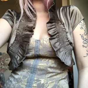 Kort beige bolero med volang - Säljer en kort bolero i glansigt beige tyg med volangkant 