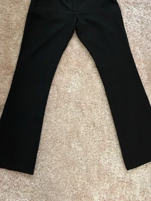 Svarta kostymbyxor från BikBok - Klassiska svarta kostymbyxor från BikBok i storlek 38. Low waist. Byxorna har raka ben, bälteshällor och två fuskfickor bak. Perfekta till en clean och stilren look. Materialet känns mjukt och följsamt.