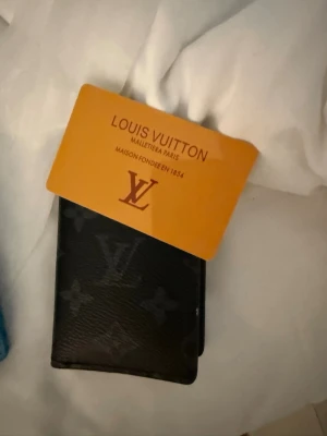 Louis Vuitton svart plånbok - Säljer en svart plånbok från Louis Vuitton med klassiskt monogrammönster. Plånboken är tillverkad i skinn och har en stilren och lyxig känsla. Perfekt för dig som vill ha något exklusivt i fickan.