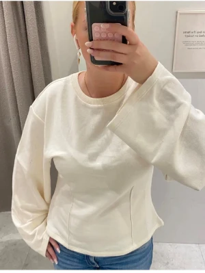 Vit tröja med vida ärmar - Säljer en stilren vit tröja med rund hals och extra vida, långa ärmar. Tröjan har en lätt figursydd passform och är gjord i mjuk bomull. Perfekt för dig som gillar en enkel men trendig look.