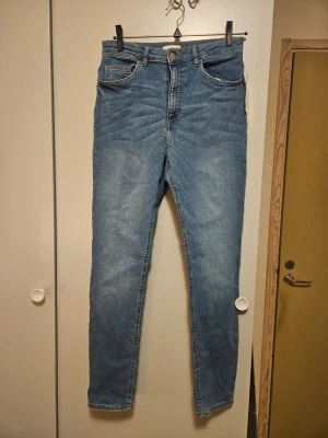 Blå super strech jeans från H&M, strl 42 - Säljer ett par klassiska blå skinny jeans från H&M i storlek 42. Jeansen har fem fickor, bälteshällor och dragkedja med knapp. Snygg tvättad look och smal passform som sitter tajt längs benen. Perfekta till sneakers eller boots.