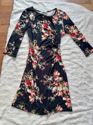 Blommig svart klänning från Oasis - Supersnygg svart klänning från Oasis med färgglatt blommönster i rött, vitt, rosa och blått. Modellen har trekvartsärm, rund halsringning och lätt rynkning i midjan för en smickrande siluett. Mjuk och stretchig i materialet, perfekt för dig som gillar en feminin vibe.