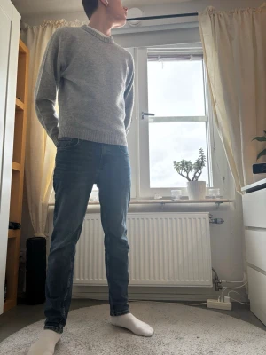 Grå stickad tröja med rund hals - En stilren grå stickad tröja med rund halsringning och ribbade muddar. Perfekt för lager-på-lager och funkar till både jeans och chinos. Enkel och klassisk design som passar till många olika outfits.