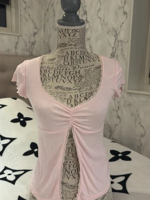 Ljusrosa omlottopp med slits - Söt ljusrosa topp med omlottdesign och djup v-ringning. Toppen har korta ärmar, rynkdetalj framtill och en slits som ger en unik look. Tillverkad i mjukt bomullsmaterial och har fina spetsdetaljer längs kanterna.