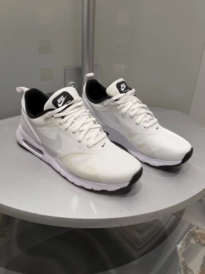 Vita Nike Air Max Tavas sneakers - Fräscha vita Nike Air Max Tavas sneakers med svart innersula och klassisk swoosh på sidan. Skorna har snörning, ventilerande mesh och synlig luftbubbla i sulan för extra komfort. Perfekta för dig som gillar stilrena och sportiga vibes.