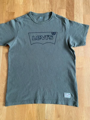  Levi's t-shirt  - Säljer en olivgrön t-shirt från Levi's med stor svart logga på bröstet och en liten patch nertill. Klassisk passform och rund halsringning. Tillverkad i 100% bomull för skön känsla och andningsförmåga. Perfekt till jeans eller shorts. Bröstvidd:47,5  Längd:65