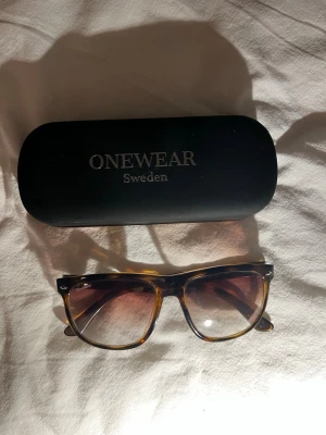 Solglasögon från Onewear - Säljer ett par stilrena solglasögon från Onewear Sweden med brunmelerad båge och glas. Ser exakt ut som raybans förutom att det är onewear som märke. Bra skick förut liten repa som man ej ser vid användning inte ens på sommaren. Använda lite. Mitt pris 299kr. Kontakt mig om du har frågor.
