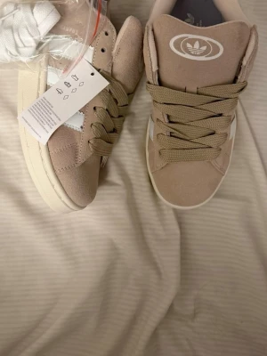Beige Adidas Campus sneakers mocka - Snygga beige Adidas Campus sneakers i mocka med klassiska vita ränder på sidorna och beige snörning. Skorna har en platt sula och rund tå, samt Adidas-logga OBS har tyvärr inte skor box 😀