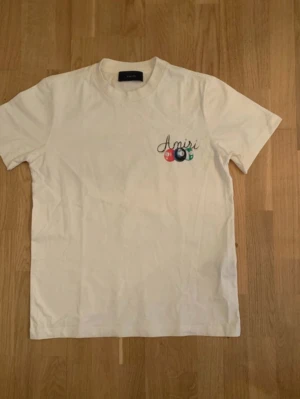 Vit Amiri t-shirt med biljardtryck - Säljer en vit t-shirt från Amiri med färgglatt biljardmotiv och text både fram och bak. T-shirten har normal passform, korta ärmar och är gjord i mjuk bomull. Perfekt för dig som gillar streetwear och unika prints.