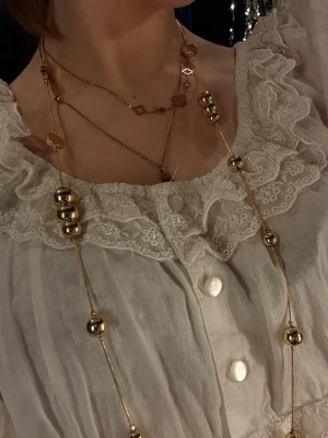 Långt halsband med guldfärgade kulor - Säljer ett långt halsband med stora och små guldfärgade kulor på tunn kedja. Halsbandet har en modern och trendig look. Perfekt accessoar för att lyfta din outfit.