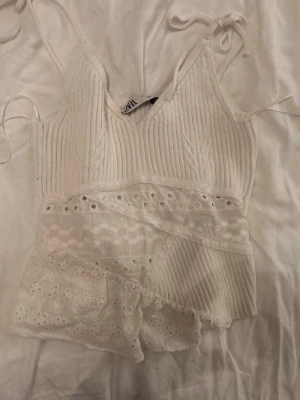 Vit spetsdetaljerad linnetopp Zara - Supersöt vit linnetopp från Zara med ribbad struktur upptill och spetsdetaljer samt broderade blommor nedtill. Tunna axelband med knyt och v-ringad halsringning. Perfekt för sommarens alla tillfällen! I storlek s. Säljer då jag aldrig använt den och inte är min stil längre!