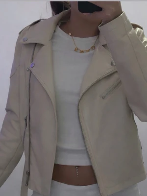 beige skinnjacka  - Snygg beige skinnjacka från Noisy May i klassisk bikerstil med silvriga dragkedjor och detaljer. Jackan har lång ärm, bred krage och snedställd dragkedja framtill. Perfekt för att lyfta vilken outfit som helst.