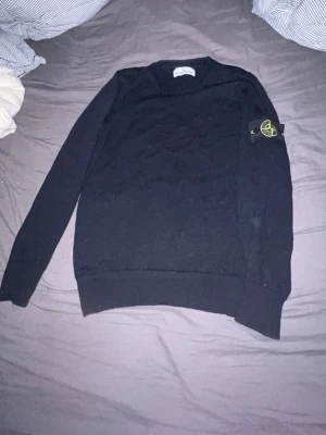  mörk blå stickad Stone Island tröja - Säljer en mörk blå stickad tröja från Stone Island med den klassiska loggan på vänster ärm. Tröjan har rund hals, lång ärm och en clean, slim passform som sitter snyggt på kroppen. Perfekt för allt och riktigt fet. Priset är inte hugget i sten!