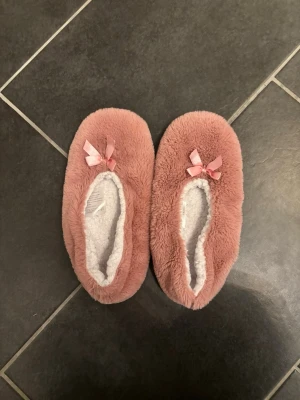 Rosa fluffiga ballerinatofflor med rosett - Supermysiga rosa ballerinaskor med vit mjuk insida. Dekorerade med en söt liten rosett framtill. Perfekta för att hålla fötterna varma hemma under kyliga dagar. Storlek 39-41