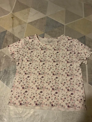 ~Blommig ribbad t-shirt från My Wear🌸 - Supersöt ribbad t-shirt från My Wear med blommigt mönster i lila och rosa på vit botten. Kortärmad modell med rund halsringning och mjukt, stretchigt material som sitter skönt. Perfekt för dig som gillar en söt och chill stil.🌺