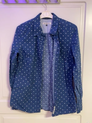 Blå prickig skjorta från Cheap Monday - Blå skjorta från Cheap Monday med vita prickar och klassisk krage. Skjortan har lång ärm och knäppning framtill. Perfekt för dig som gillar mönster och vill sticka ut lite extra.