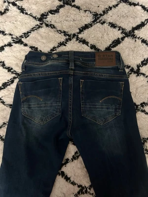 Mörkblå G-Star Midge jeans💙💙 - Snygga mörkblå jeans från G-Star, modell Midge. Klassisk femficksdesign med kontrastsömmar och G-Star-logga på fickan. Jeansen är bootcut och är mid waist. Waist:24 Längd:32