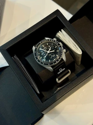 Omega x Swatch MoonSwatch klocka - Säljer en Omega x Swatch MoonSwatch Mission to the Moon. Klockan har svart urtavla med vita detaljer, tachymeter och svart textilband med Omega-logga. Boetten är i biokeramik och designen är inspirerad av klassiska Speedmaster. Kommer i originalförpackning.